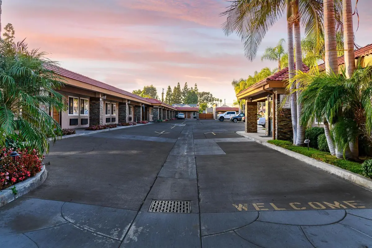a parking lot with a welcome message on the ground, surrounded by palm trees and a building with a red roof