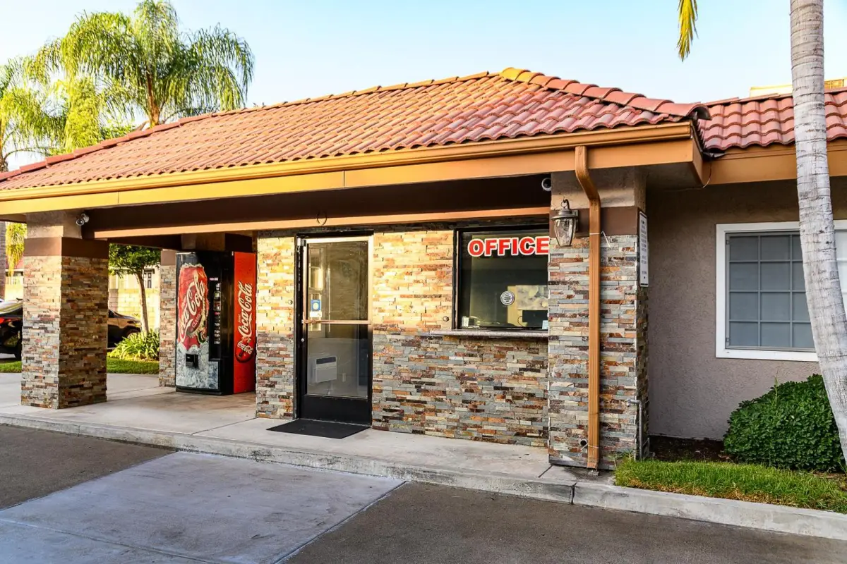 A building with a tiled roof and stone facade has a covered entrance with a vending machine and an office window.